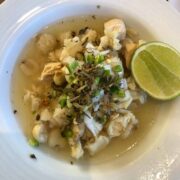 chicken pozole in a white bowl with oregano, onion, and a lime wedge