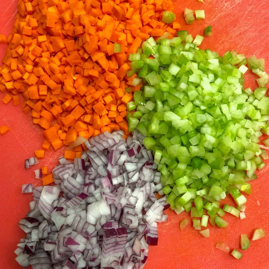 diced carrots, onion and celery also known as mirepoix on a cutting board