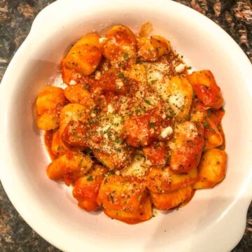 potato gnocchi with an arrabbiata sauce garnished with parsley and parmesan in a white bowl.