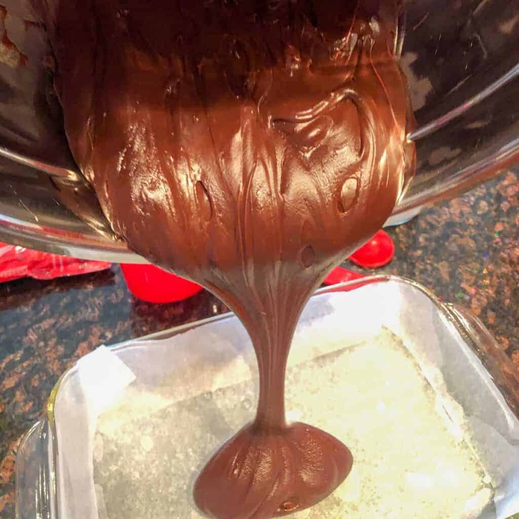 pouring the homemade fudge mixture into a baking dish to firm up.