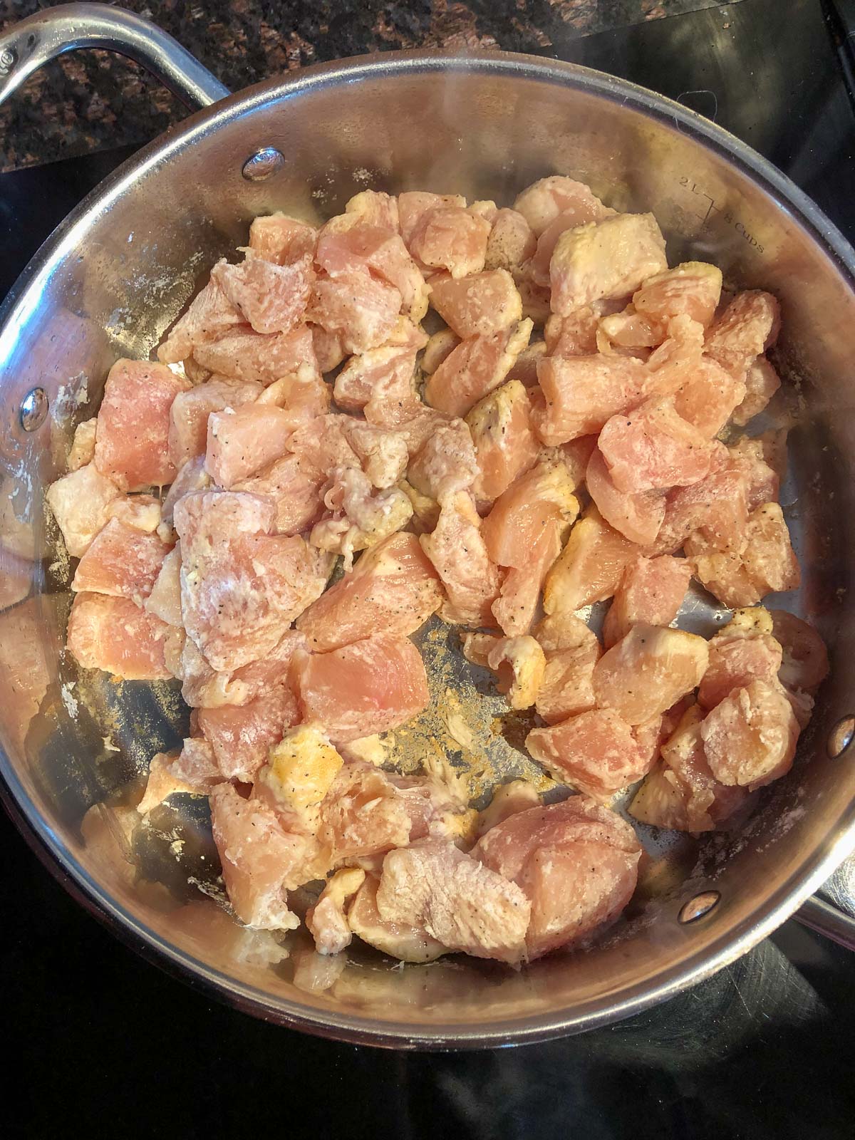 cornstarch dusted chicken cooking in a stainless steel skillet