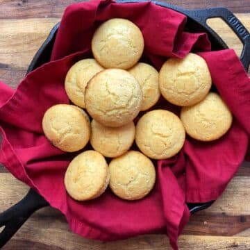 golden brown cornbread muffins in a red linen lined cast iron skillet on a wood background