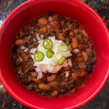 bowl of chili with beans topped with sour cream and serrano pepper slices