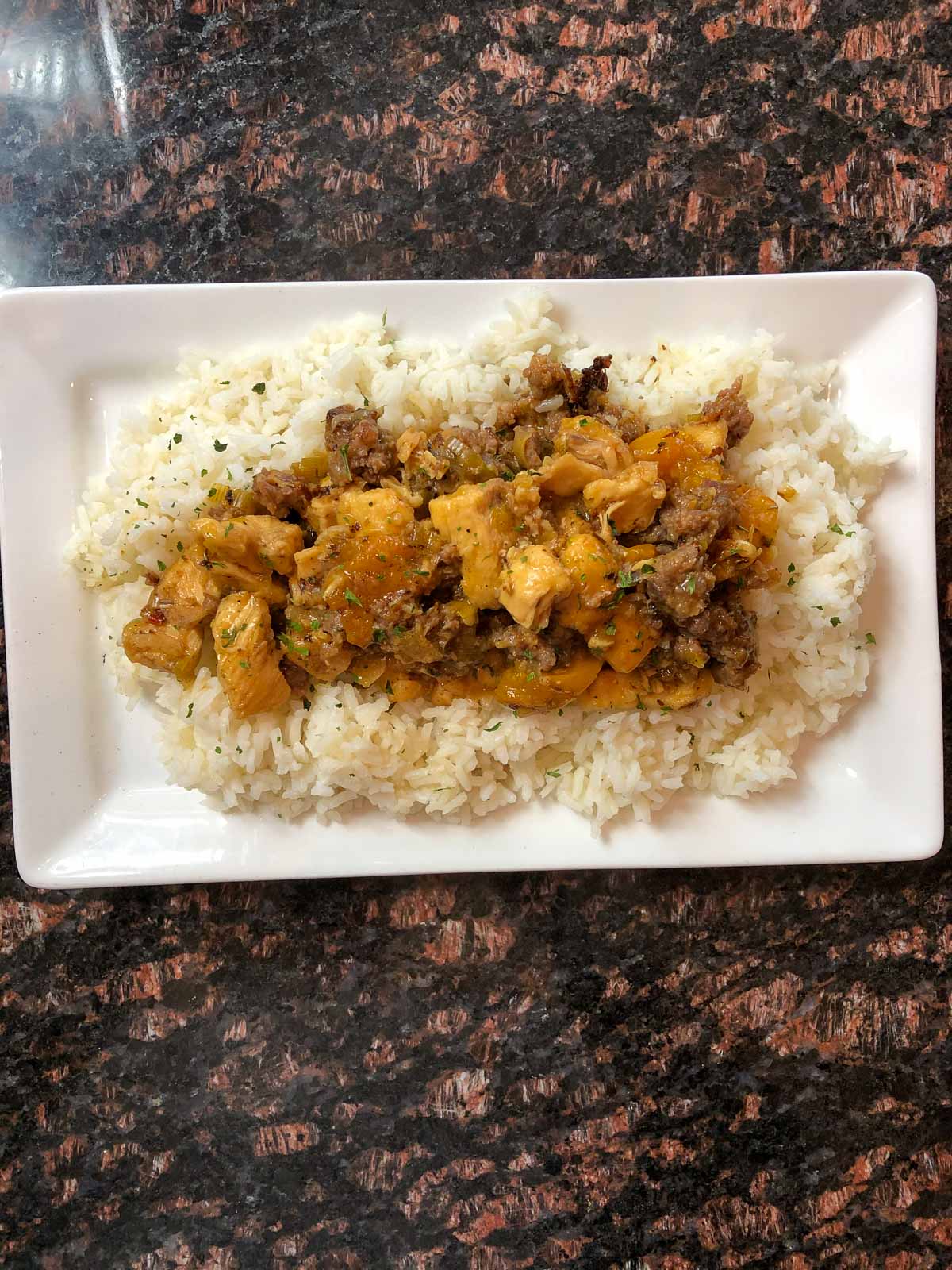 top view of chicken and sausage dish known as sweet and sour chicken sitting on a white plate on a marble counter.