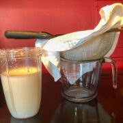 homemade coconut milk in a blender sitting next to a napkin lined strainer