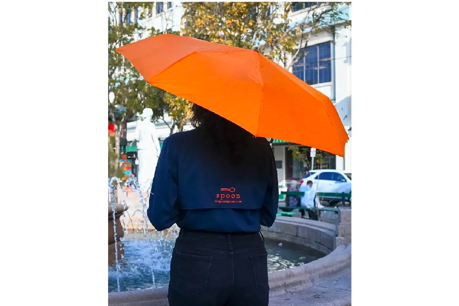 image of a person holding an orange umbrella with a shirt displaying The Spoon Experience.